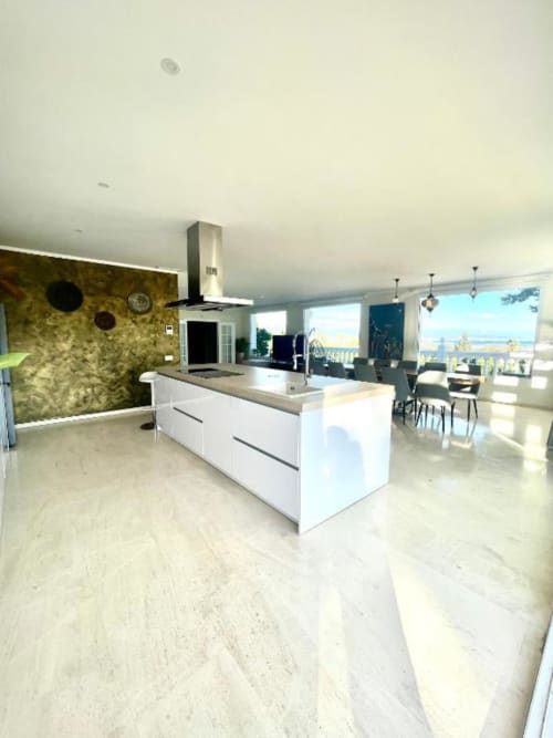Cocina de villa moderna con isla blanca, vistas al océano y acceso a terraza en Villa Magos Málaga