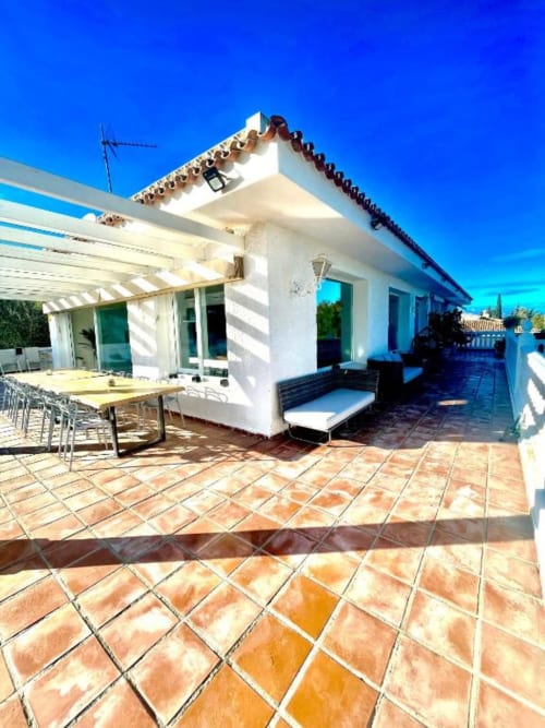 Terraza de terracota Villa Magos con villa blanca, pérgola, comedor y vistas al océano en Málaga