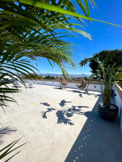 Soleada terraza en la azotea de Villa Magos en Málaga con plantas de palma, sillas colgantes, vistas a la montaña y zona de descanso