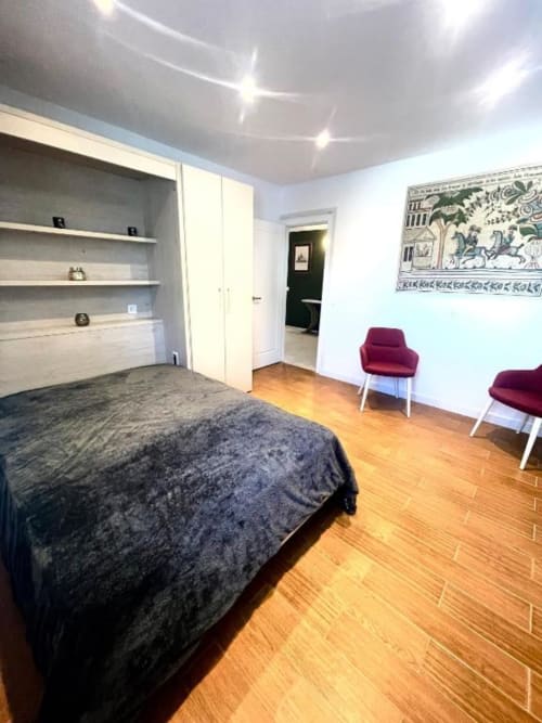 Dormitorio moderno de la Villa Magos, Málaga: cama, estanterías integradas, sillas burdeos, suelos de madera y vistas al océano