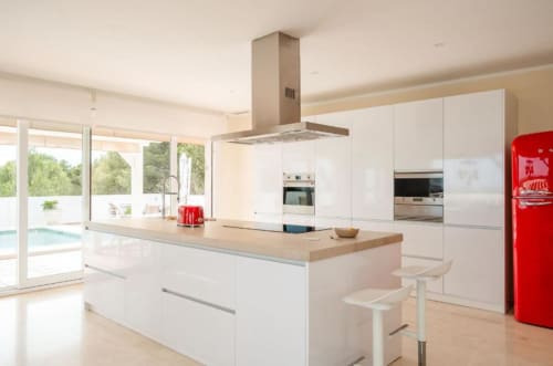 Moderna cocina blanca con isla, refrigerador rojo y vistas a la piscina en Villa Magos, Málaga