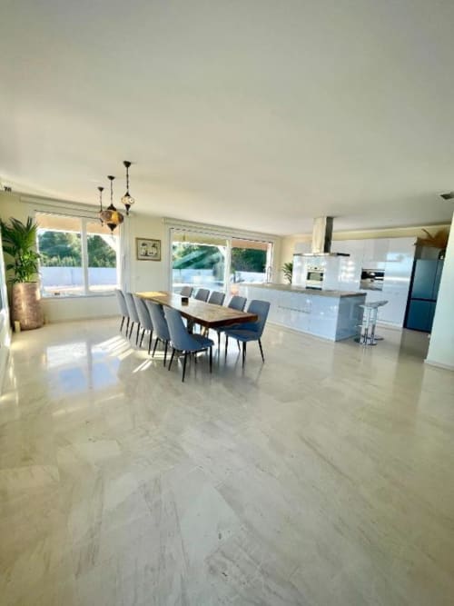Cocina y comedor moderno con vistas al océano, muebles blancos y sillas azules en mesa de madera en Málaga