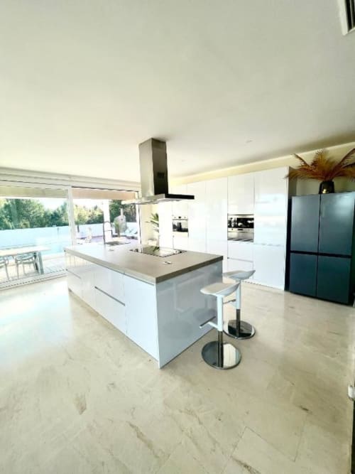 Cocina moderna de villa con isla, muebles blancos, refrigerador oscuro y terraza con vistas a piscina y océano en Málaga