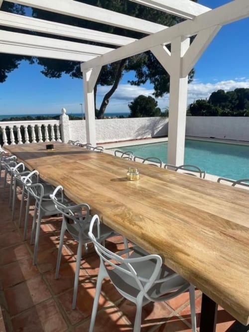 Mesa de comedor de madera con sillas blancas en terraza con vistas a la piscina y océano en Villa Magos, Málaga