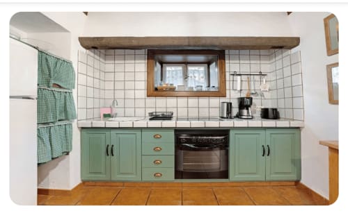 Cocina verde salvia con azulejos blancos tipo metro, encimera de madera, horno negro y ventana en la villa Casa Rural La Caldera