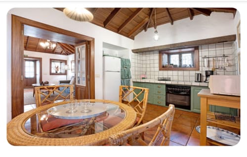 Amplia zona de cocina-comedor en villa Casa Rural La Caldera con mesa redonda de mimbre, muebles verdes y vigas de madera