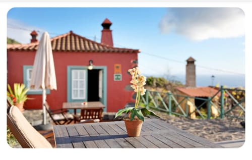 Villa roja Casa Rural La Caldera con vistas al océano, puertas con ribetes blancos, flores en macetas en terraza de madera en Fuencaliente, La