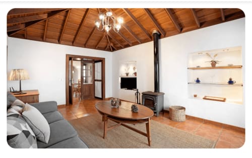 Elegante sala de estar con vigas de madera, chimenea y estanterías integradas en la villa Casa Rural La Caldera en La Palma