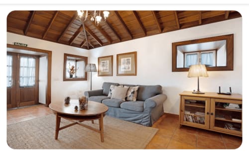 Amplia sala de estar con techo de madera, sofá gris, mesa de centro redonda y chimenea en la villa Casa Rural La Caldera