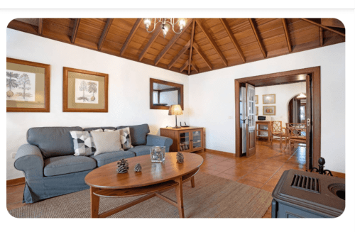 Amplio salón en villa de La Palma con sofá azul, vigas de madera, mesita ovalada y pisos de terracota