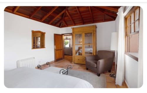 Dormitorio espacioso con techo de vigas de madera, sillón marrón y vistas al mar en Casa rural Los Llanos Negros, La Palma