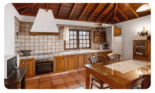 Cocina espaciosa con muebles de madera, salpicadero de azulejos beige, mesa de comedor y vigas de madera vista en villa La Palma