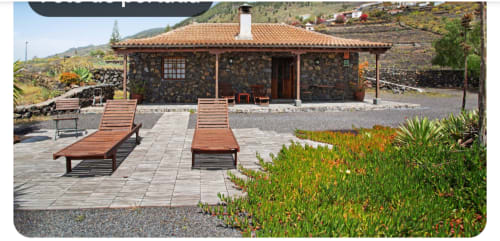 Villa rural canaria con fachada de piedra, tejado de barro, tumbonas en patio y vistas a las montañas de La Palma