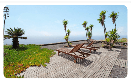 Tumbonas de madera en la terraza con vistas al océano, palmeras y jardines verdes en villa La Palma