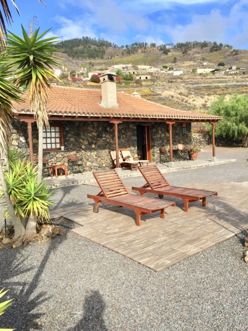 Villa de piedra rústica con tumbonas de madera en terraza, palmeras y vistas a las montañas en Fuencaliente, La Palma