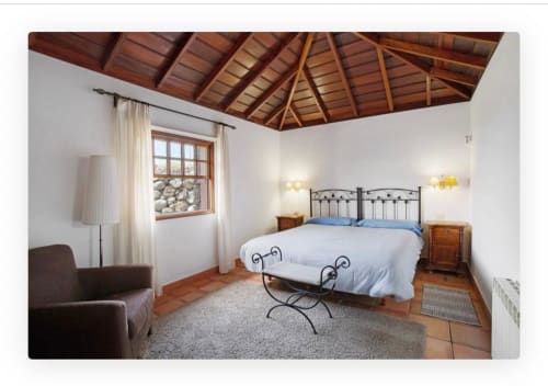 Amplia villa con dormitorio, cama de hierro forjado, vigas de madera y vistas al mar desde las ventanas en La Palma