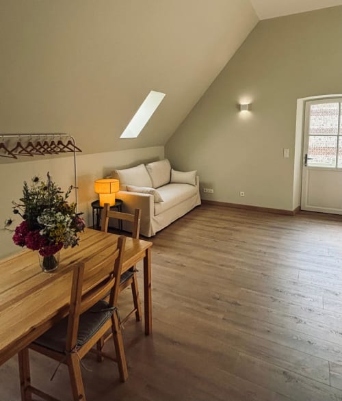 Studio lumineux dans les combles du Manoir De Daubeuf avec mobilier en bois, canapé crème, velux et parquet