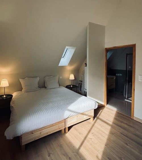 Chambre mansardée lumineuse au Manoir De Daubeuf avec lit en bois, puits de lumière et accès à la salle de bain attenante
