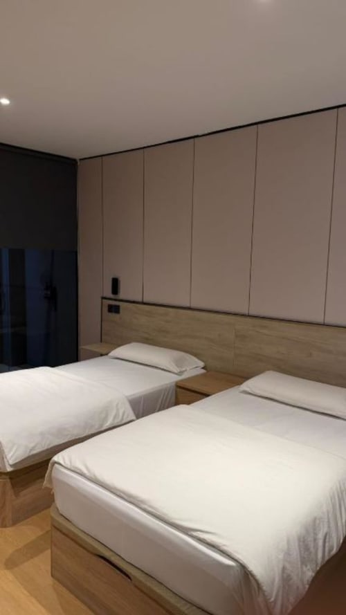 Moderna habitación doble en ITOUR Hotel de Museros con dos camas, cabecero de madera y paneles de pared beige del piso al techo