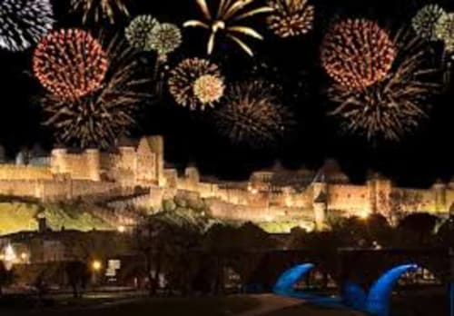 Les feux d'artifice éclatent au-dessus des remparts illuminés de la forteresse médiévale de Carcassonne avec des éléments architecturaux bleus en bas la nuit