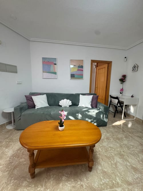 Sala de estar moderna en Haus Holiday Homes, Los Alcázares, con sofá verde, mesa de café de madera y arte mural colorido