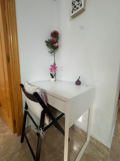 Escritorio blanco con flores rosas en jarrón y silla negra en la cabaña Haus Holiday Homes de Los Alcázares