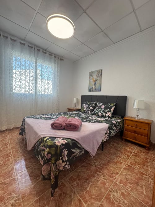 Habitación en Haus Holiday Homes de Los Alcázares con ropa de cama floral, mesita de noche de madera y luz de techo