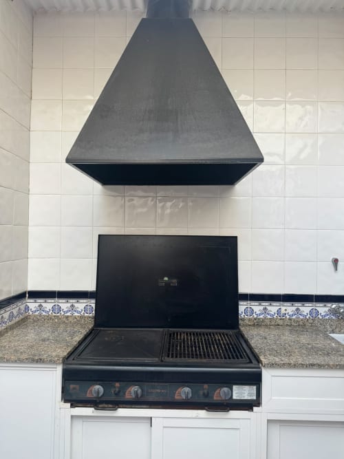Cocina negra con estufa y plancha bajo campana extractora en la casita Los Alcázares