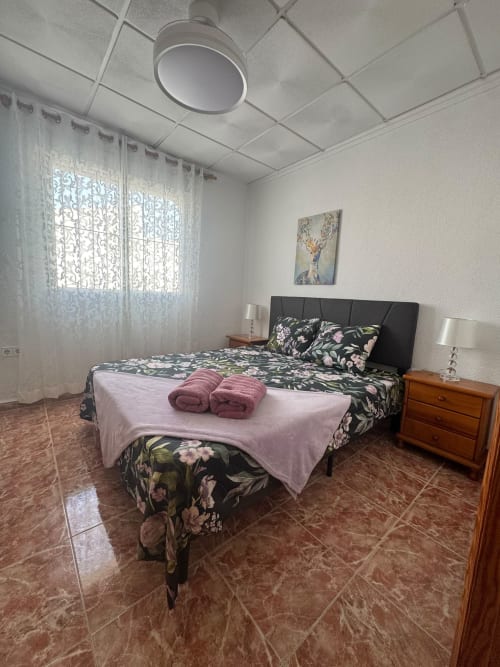 Dormitorio luminoso en Haus Holiday Homes, Los Alcázares, con cama queen, ropa de cama floral, mesillas de madera y diseño estampado