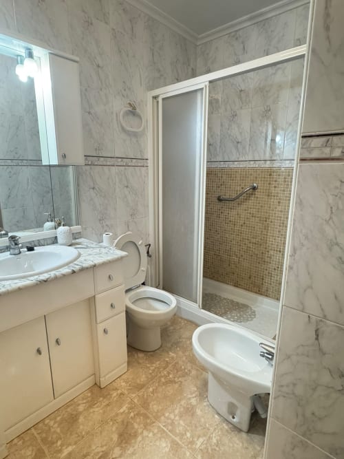 Baño moderno con azulejos de mármol, lavamanos, inodoro y ducha abierta en la casa de vacaciones cerca de Los Alcázares