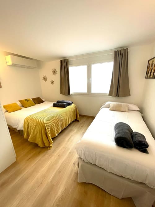 Dormitorio luminoso en Villa Magos B&B en Málaga con dos camas, ropa de cama amarilla, suelo de madera y grandes ventanales