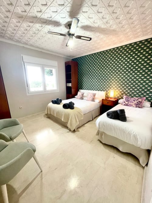 Moderna habitación doble en Villa Magos B&B en Málaga con pared de acento texturizada en verde, camas blancas y ventilador de techo