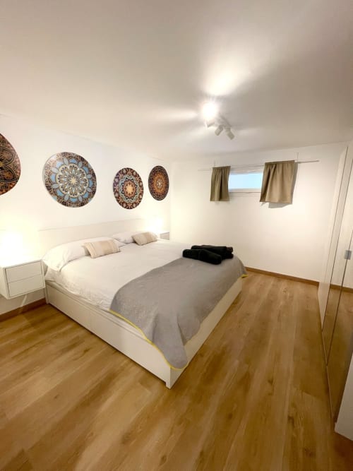 Dormitorio luminoso en Villa Magos B&B de Málaga con cama blanca, suelo de madera y platos decorativos en la pared