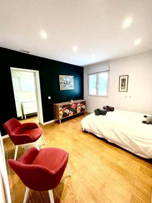 Dormitorio moderno en Villa Magos Málaga con pared de acento oscuro, sillas rojas, pisos de madera y mobiliario contemporáneo