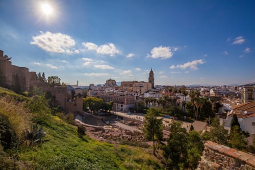 Paisaje urbano de Málaga con catedral y edificios de terracota, ladera verde en primer plano de Villa Magos