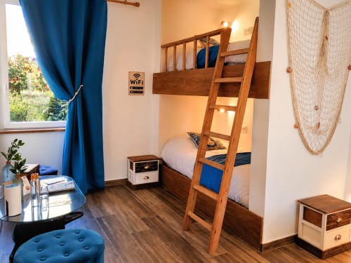 Chambre douillette avec lits superposés à La Synchronicité BnB à Saint Sauveur, échelle en bois, rideaux bleus et vue sur le jardin