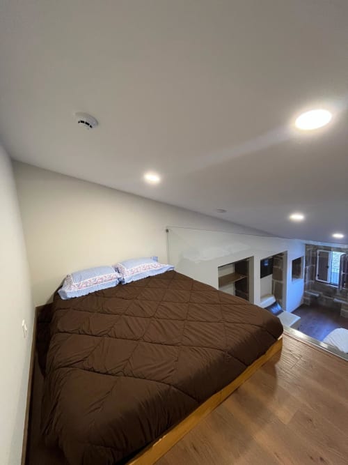 Quarto Bersford com cama estofada marrom, almofadas azuis, piso de madeira, iluminação embutida e espaço de armazenamento integrado