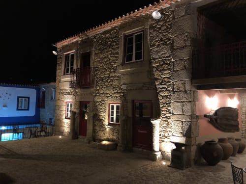 Edifício histórico de pedra iluminado à noite com luz quente, telhado em terracota, portas de madeira e arquitetura portuguesa tradicional