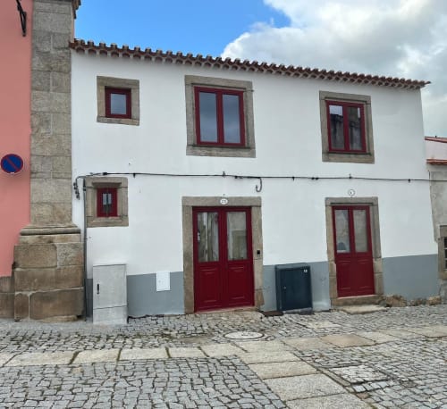 Edifício histórico português com paredes brancas, portas e caixilhos vermelhos, entrada de pátio em calçada à portuguesa