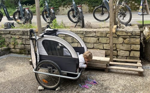 Child in bike trailer at Maison Lapopie, Saint-Cirq-Lapopie, with e-bikes parked behind stone wall