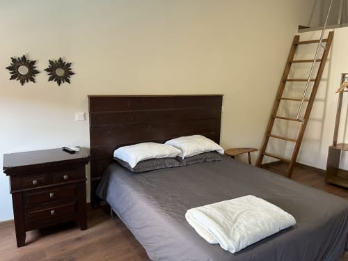 Quarto em RISOTURISMO com cama de madeira escura, almofadas brancas, criado-mudo, espelhos decorativos e escada de madeira