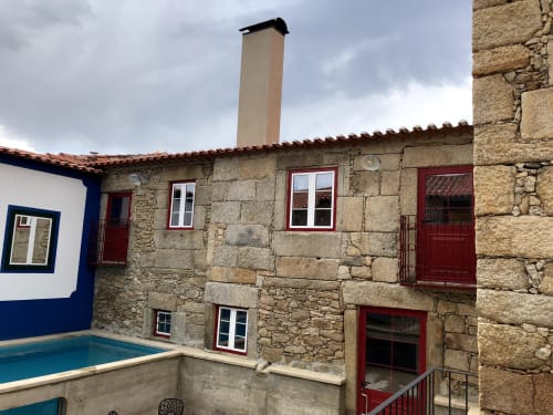 Historic stone Portuguese manor house with red doors and windows, chimney, courtyard pool