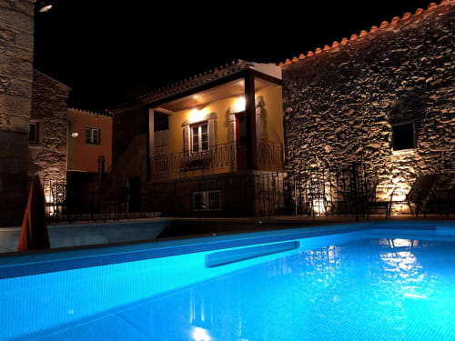 Illuminated Portuguese colonial house with stone walls overlooking glowing blue swimming pool at night, Quinta das Pias hotel