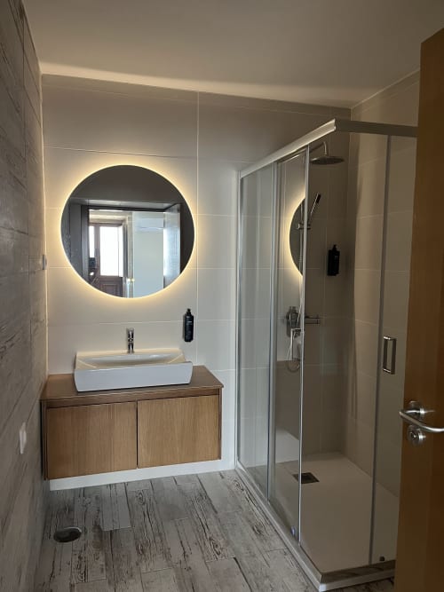 Modern bathroom in Quarto Wellington at RISOTURISMO with illuminated round mirror, vessel sink, wooden vanity, and walk-in