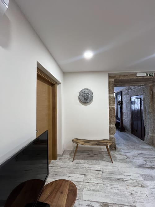 Modern hallway in Quarto Wellington at RISOTURISMO with wooden bench, metallic bust sculpture, and stone corridor leading to