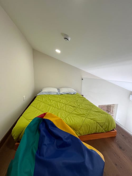 Quarto luminoso em Quarto Junot na RISOTURISMO com roupa de cama verde limão, almofadas brancas e tenda colorida no piso de madeira