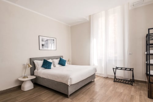 Camera moderna nella Flavia's Holiday Home a Roma con letto grigio, biancheria bianca, cuscini turchesi, pavimento in legno e ampie finestre