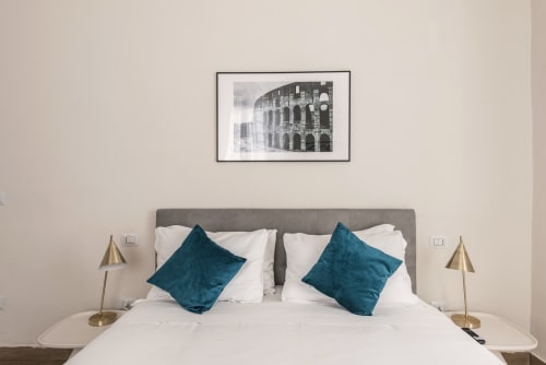 Camera moderna a Flavia's Holiday Home a Roma con testata grigia, biancheria bianca, cuscini turchesi, lampade in ottone e cornici