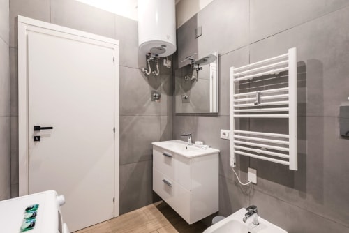 Bagno moderno nella casa vacanze di Flavia a Roma con vanità bianca, scaldasalviette, piastrelle grigie e soffione a pioggia.