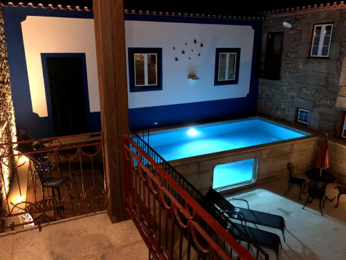 Piscina do pátio iluminada à noite com luzes azuis, edifícios em pedra e zona de estar em quinta rural portuguesa
